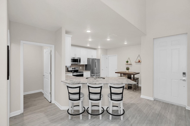 kitchen featuring light stone countertops, stainless steel appliances, light hardwood / wood-style floors, white cabinetry, and a breakfast bar