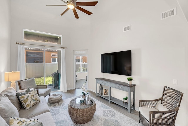 living room with a towering ceiling, light hardwood / wood-style floors, and ceiling fan