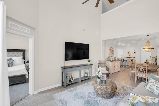 living room featuring ceiling fan, light wood-type flooring, and a towering ceiling