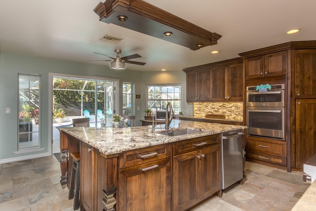 kitchen featuring light tile flooring, backsplash, stainless steel appliances, a center island with sink, and ceiling fan