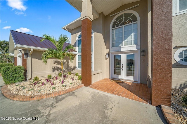 entrance to property with french doors, metal roof, a standing seam roof, and stucco siding