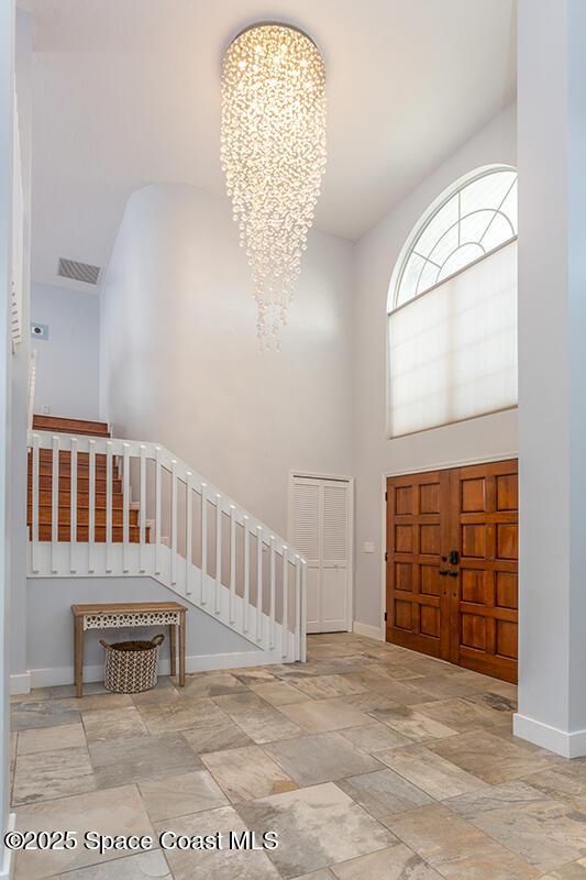 foyer featuring a high ceiling, baseboards, stairway, stone finish floor, and an inviting chandelier