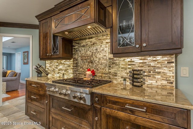 kitchen featuring light stone counters, stainless steel gas cooktop, backsplash, glass insert cabinets, and custom range hood