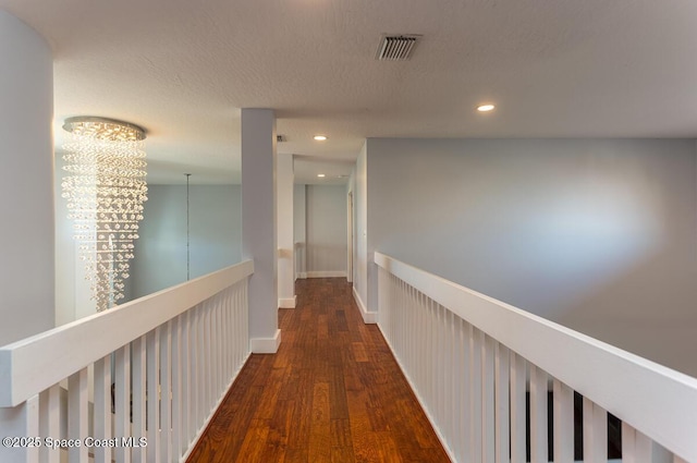 corridor featuring a textured ceiling, recessed lighting, dark wood-style flooring, visible vents, and baseboards