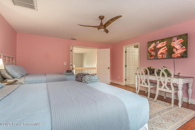 bedroom featuring a ceiling fan, wood finished floors, visible vents, and baseboards