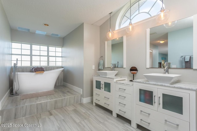 bathroom with double vanity, a soaking tub, a sink, and baseboards