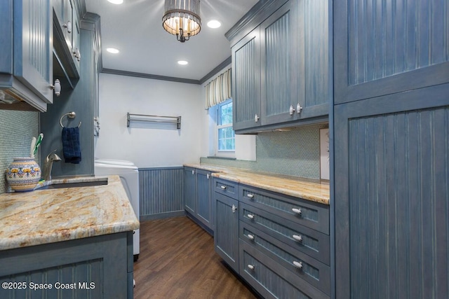 kitchen with a wainscoted wall, dark wood finished floors, backsplash, ornamental molding, and light stone countertops