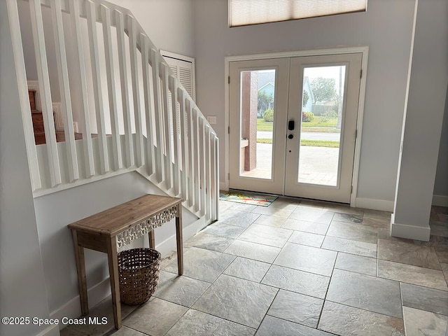 entryway with stone tile floors, stairs, baseboards, and french doors