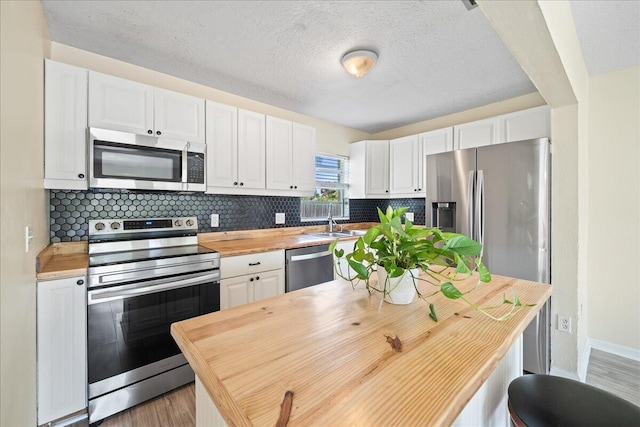 kitchen featuring appliances with stainless steel finishes, butcher block countertops, tasteful backsplash, and light wood-type flooring