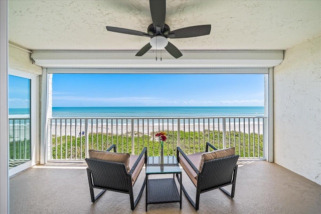 sunroom / solarium with a water view, plenty of natural light, ceiling fan, and a view of the beach