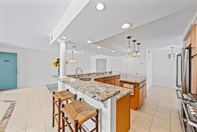 kitchen featuring decorative light fixtures, decorative columns, light tile floors, a breakfast bar area, and a kitchen island