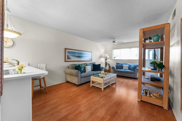 living room with a textured ceiling, wood-type flooring, sink, and ceiling fan