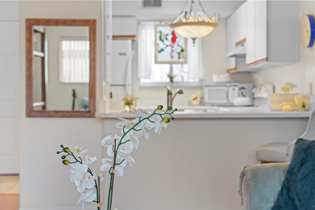 kitchen with range hood, hanging light fixtures, white appliances, and white cabinetry