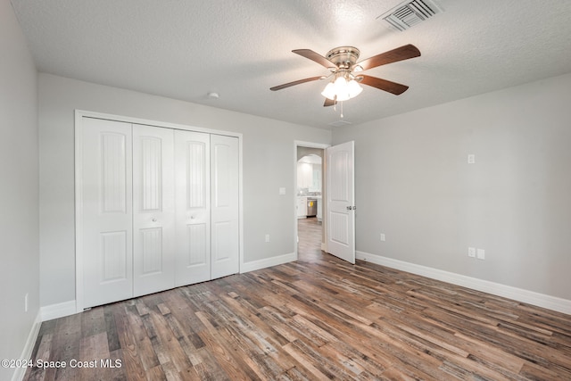 unfurnished bedroom with a textured ceiling, ceiling fan, a closet, and dark hardwood / wood-style floors