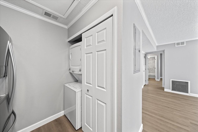 laundry room with ornamental molding, stacked washer / drying machine, hardwood / wood-style flooring, and a textured ceiling