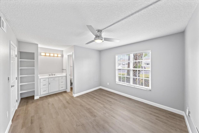 unfurnished bedroom featuring light hardwood / wood-style flooring, ceiling fan, connected bathroom, and a textured ceiling