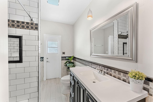 bathroom featuring vanity, toilet, tiled shower, and tile walls