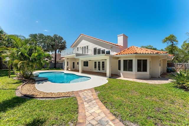 rear view of property featuring french doors, a balcony, a patio, a fenced in pool, and a lawn