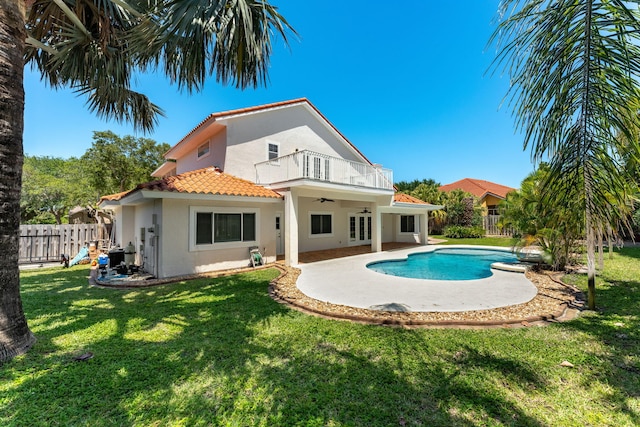 rear view of property with a yard, a balcony, ceiling fan, and a fenced in pool