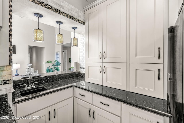 kitchen with dark stone countertops, white cabinetry, sink, and tasteful backsplash