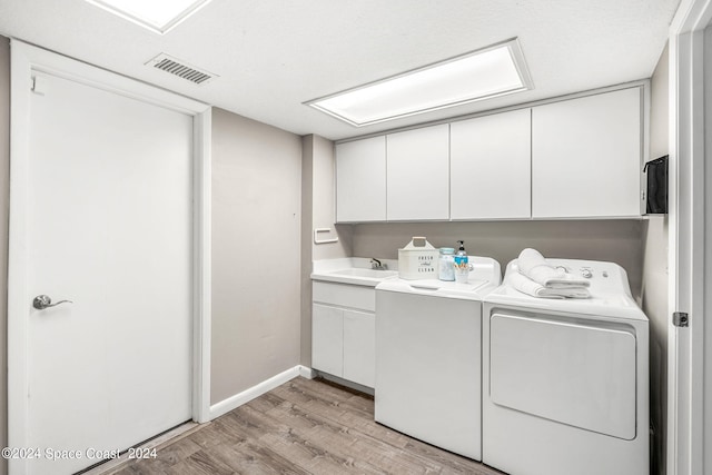 washroom with cabinets, washing machine and clothes dryer, sink, and light hardwood / wood-style flooring