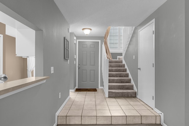 foyer with a textured ceiling, light tile patterned floors, stairs, and baseboards