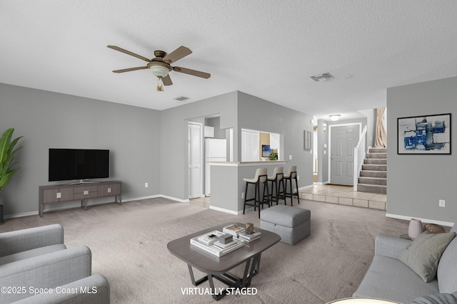 living room featuring light colored carpet, visible vents, stairway, ceiling fan, and a textured ceiling