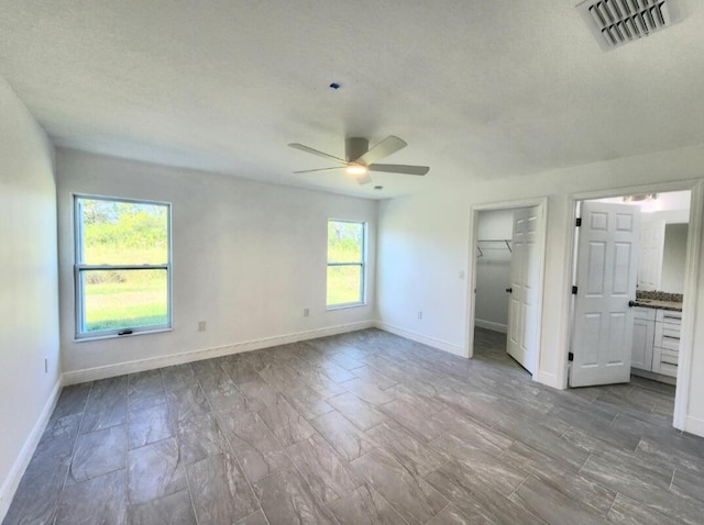 unfurnished bedroom with connected bathroom, ceiling fan, a textured ceiling, and multiple windows