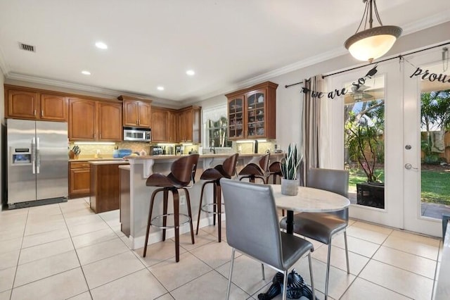 kitchen with a kitchen bar, backsplash, stainless steel appliances, light tile flooring, and ornamental molding