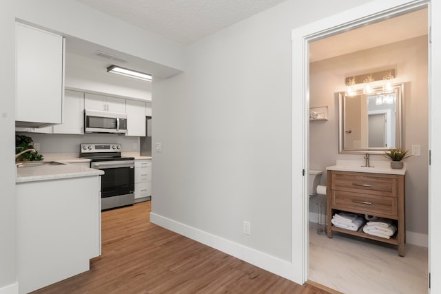 kitchen featuring sink, appliances with stainless steel finishes, white cabinetry, and hardwood / wood-style floors