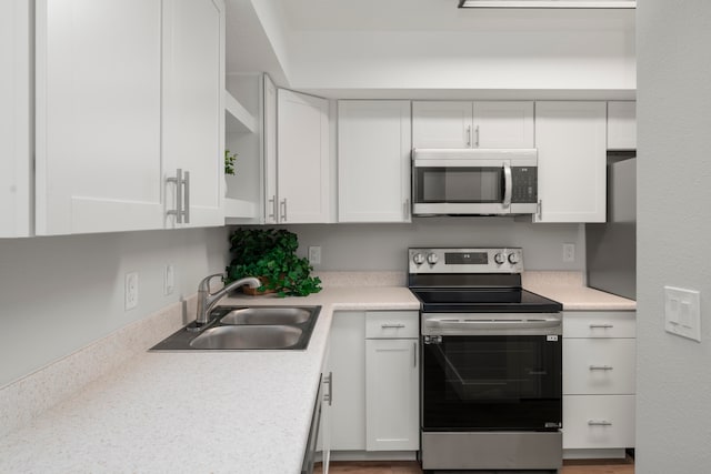 kitchen with hardwood / wood-style flooring, appliances with stainless steel finishes, white cabinetry, and sink