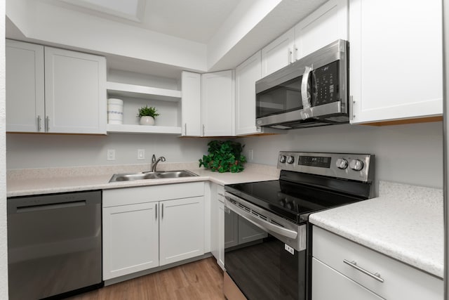 kitchen with white cabinets, sink, appliances with stainless steel finishes, and light hardwood / wood-style flooring