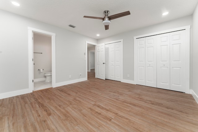 unfurnished bedroom featuring light hardwood / wood-style flooring, ceiling fan, ensuite bath, and multiple closets