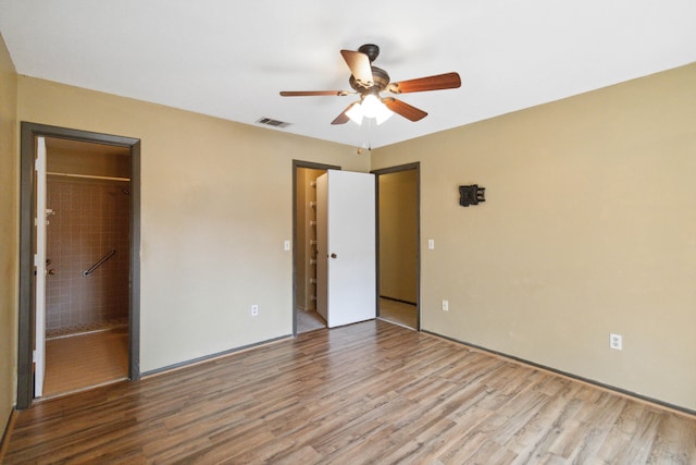 unfurnished bedroom featuring a closet, ceiling fan, hardwood / wood-style floors, connected bathroom, and a spacious closet