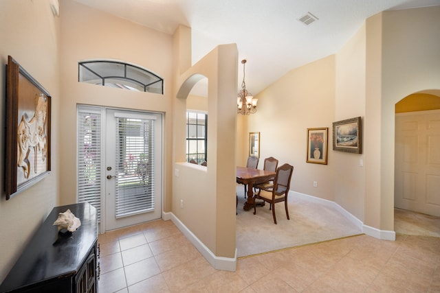 tiled foyer entrance with high vaulted ceiling, french doors, and a chandelier