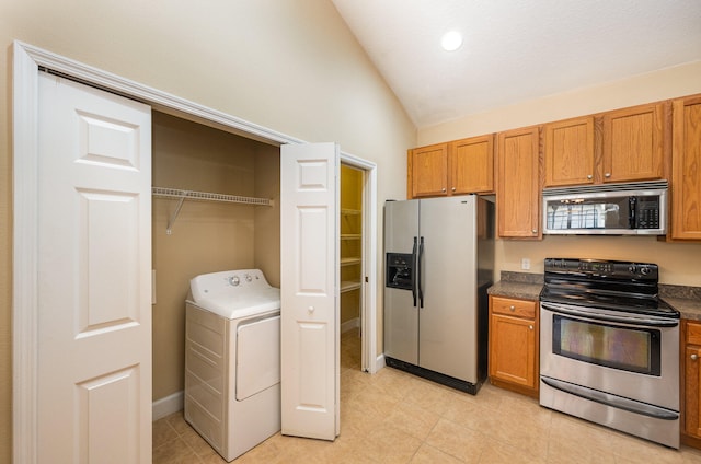 kitchen featuring appliances with stainless steel finishes, light tile floors, vaulted ceiling, and washer / dryer