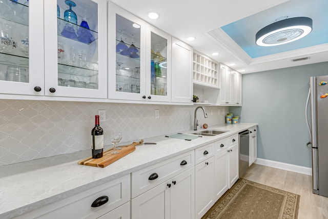 kitchen with appliances with stainless steel finishes, light hardwood / wood-style flooring, tasteful backsplash, and a raised ceiling