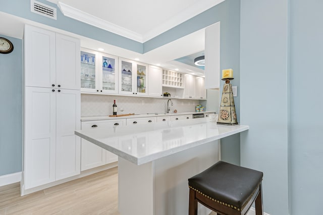 kitchen with kitchen peninsula, a kitchen bar, backsplash, light hardwood / wood-style flooring, and white cabinets