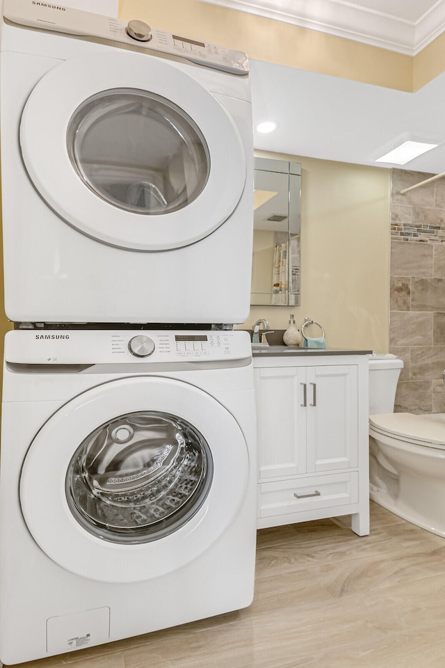 clothes washing area featuring crown molding, light hardwood / wood-style floors, and stacked washer and dryer