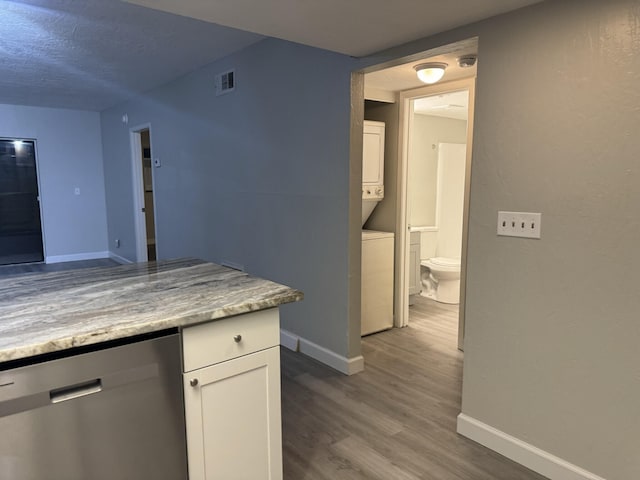 kitchen with dishwasher, hardwood / wood-style flooring, stacked washing maching and dryer, and white cabinetry