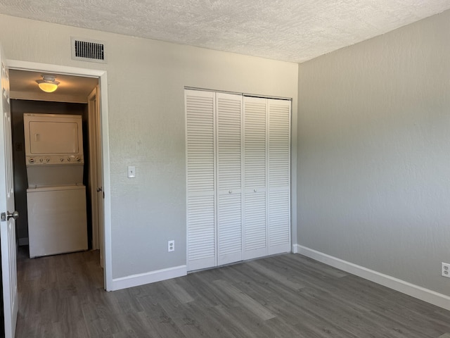 unfurnished bedroom featuring a closet, a textured ceiling, stacked washer and clothes dryer, and dark wood-type flooring