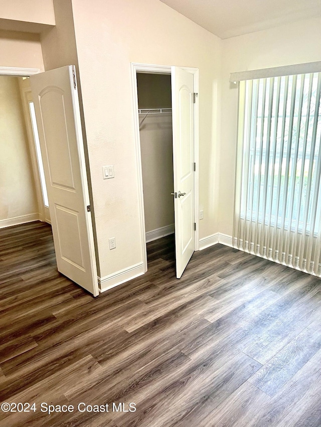 unfurnished bedroom with dark hardwood / wood-style flooring, lofted ceiling, and a closet