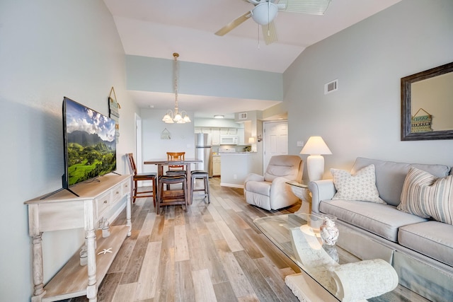 living room featuring ceiling fan with notable chandelier, light hardwood / wood-style floors, and vaulted ceiling