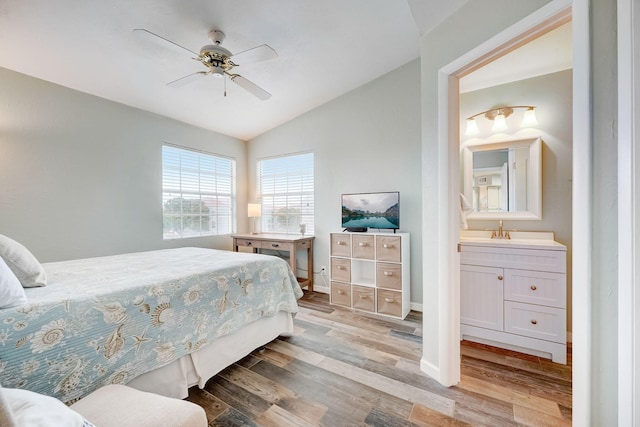 bedroom with light hardwood / wood-style flooring, vaulted ceiling, sink, connected bathroom, and ceiling fan