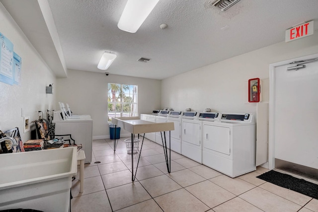 washroom with a textured ceiling, separate washer and dryer, and light tile patterned floors