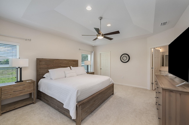 bedroom with light carpet, a tray ceiling, multiple windows, and ceiling fan