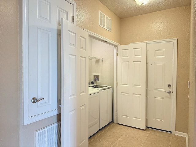 clothes washing area with a textured ceiling, washing machine and dryer, and light tile patterned floors