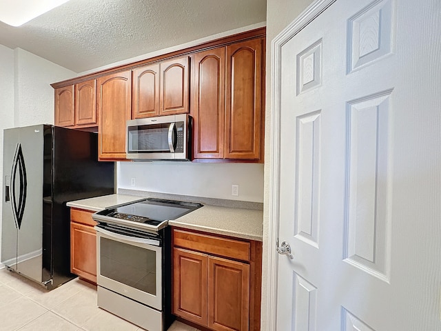 kitchen with appliances with stainless steel finishes, a textured ceiling, and light tile patterned floors