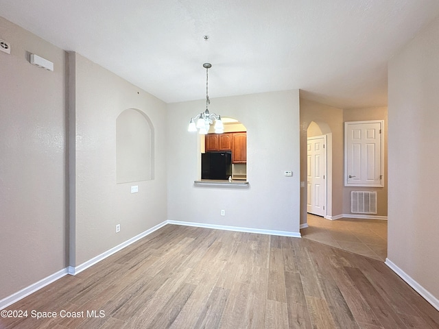 spare room featuring an inviting chandelier and light hardwood / wood-style floors