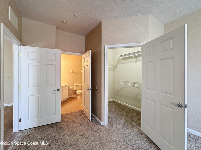 unfurnished bedroom with carpet, a walk in closet, a textured ceiling, and a closet